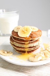 Photo of Plate of banana pancakes with honey on white wooden table
