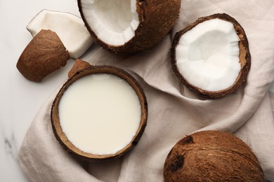 Delicious vegan milk in coconut and pieces of ripe fruit on white table, flat lay