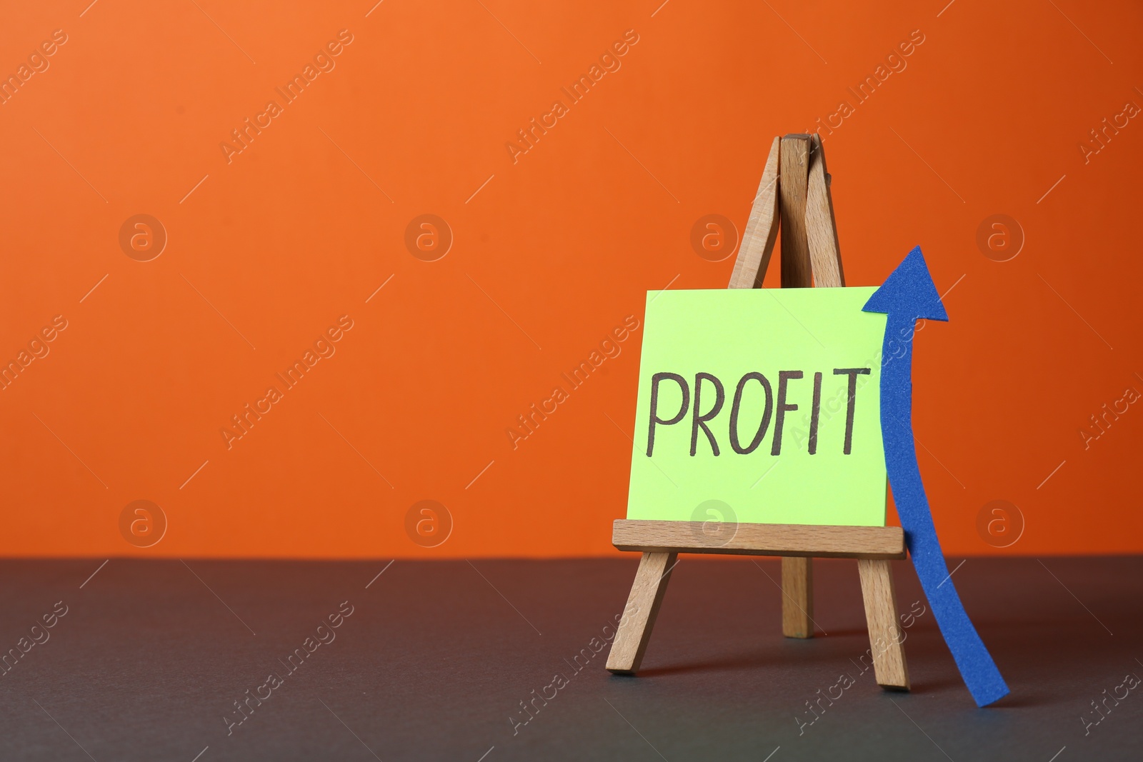 Photo of Economic profit. Easel with note and arrow on grey table against orange background, space for text