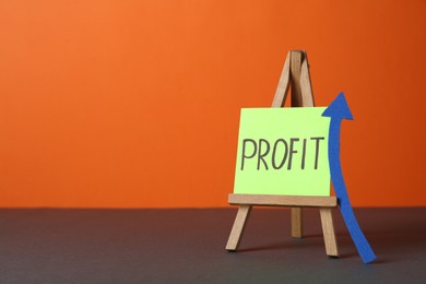 Photo of Economic profit. Easel with note and arrow on grey table against orange background, space for text