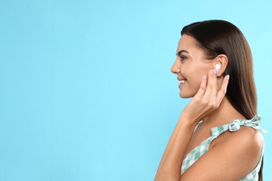 Photo of Happy young woman listening to music through wireless earphones on light blue background. Space for text