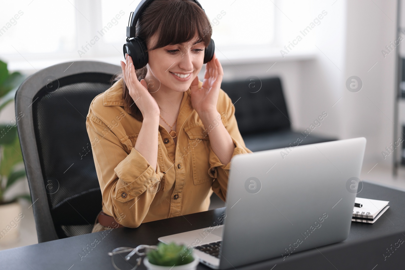 Photo of Woman in headphones watching webinar at table in office