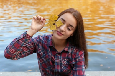Photo of Young beautiful woman with leaf near pond in park. Autumn walk