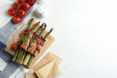 Photo of Oven baked asparagus wrapped with bacon on white wooden table, flat lay. Space for text