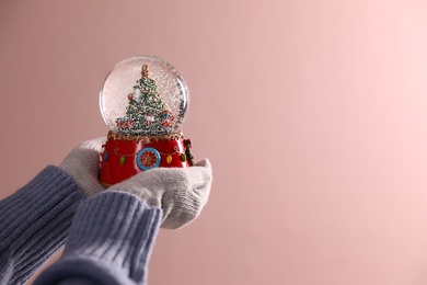 Photo of Woman holding decorative snow globe on pink background, closeup. Space for text