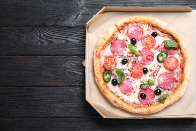 Photo of Delicious pizza Diablo in cardboard box on wooden background, top view. Space for text