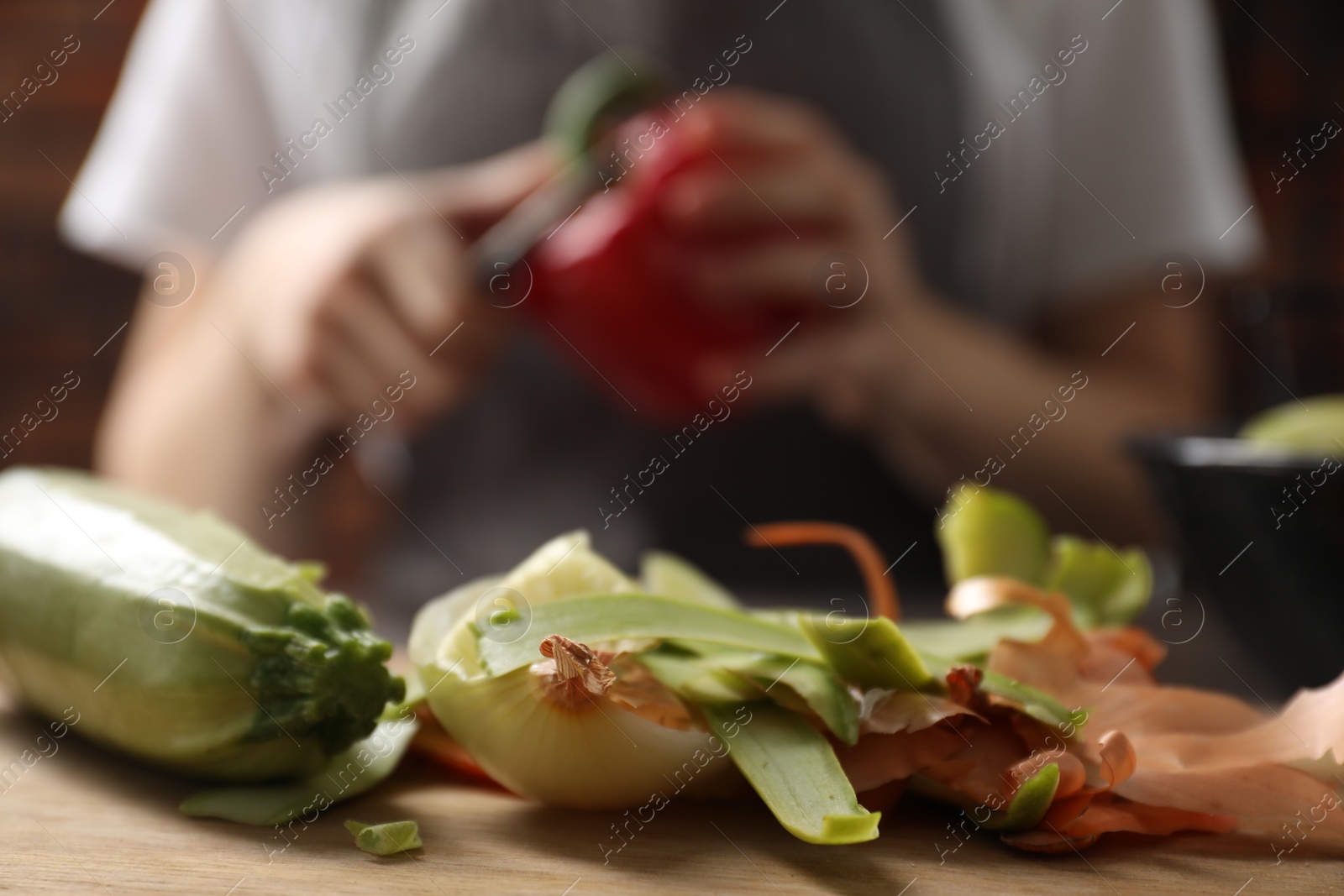 Photo of Woman with bell pepper, peels of fresh vegetables on table indoors, selective focus