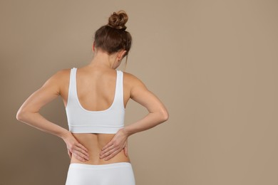 Photo of Woman suffering from pain in back on beige background. Space for text