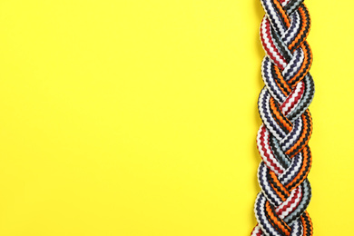 Photo of Top view of braided colorful ropes on yellow background, space for text. Unity concept