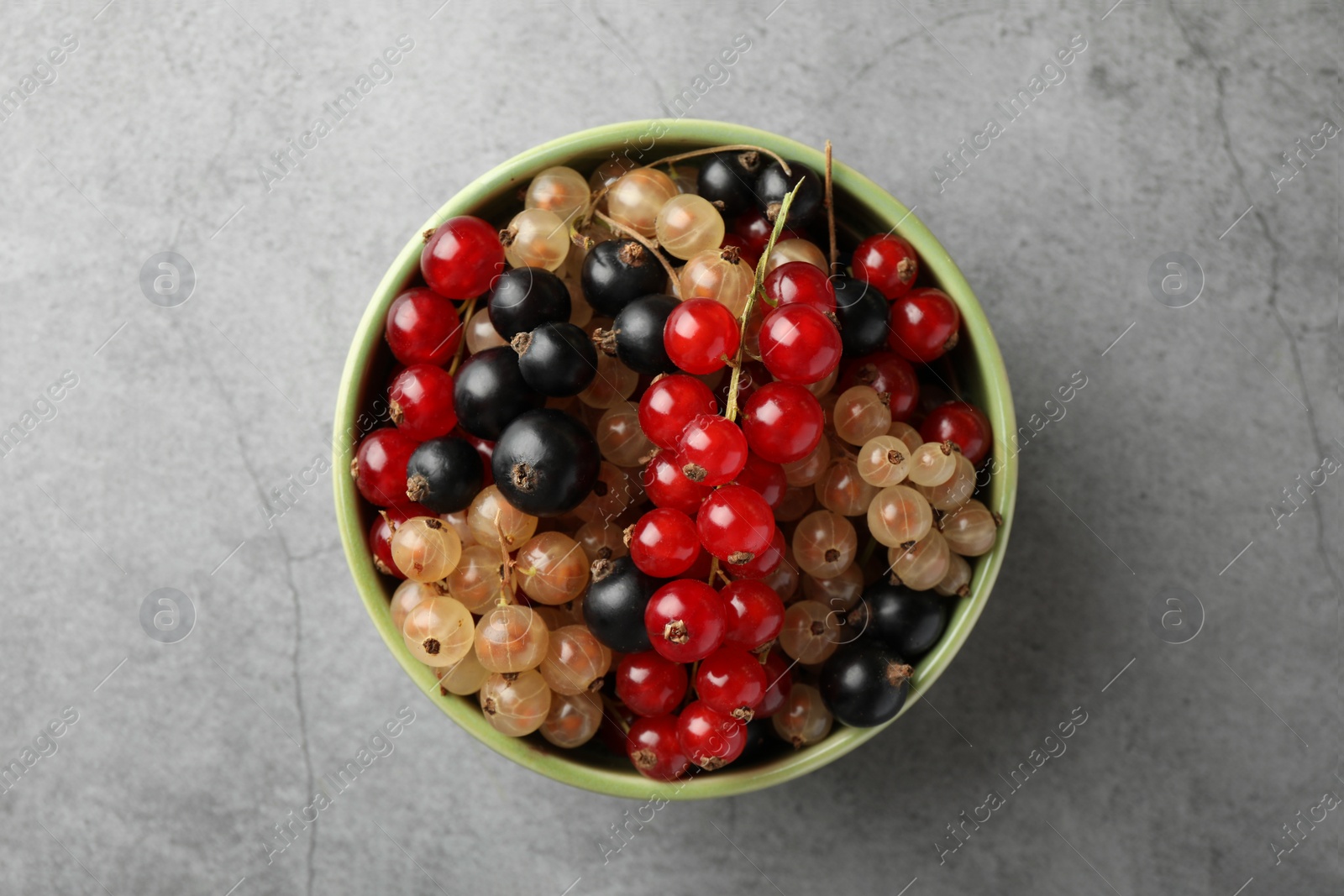 Photo of Different fresh ripe currants in bowl on light grey table, top view