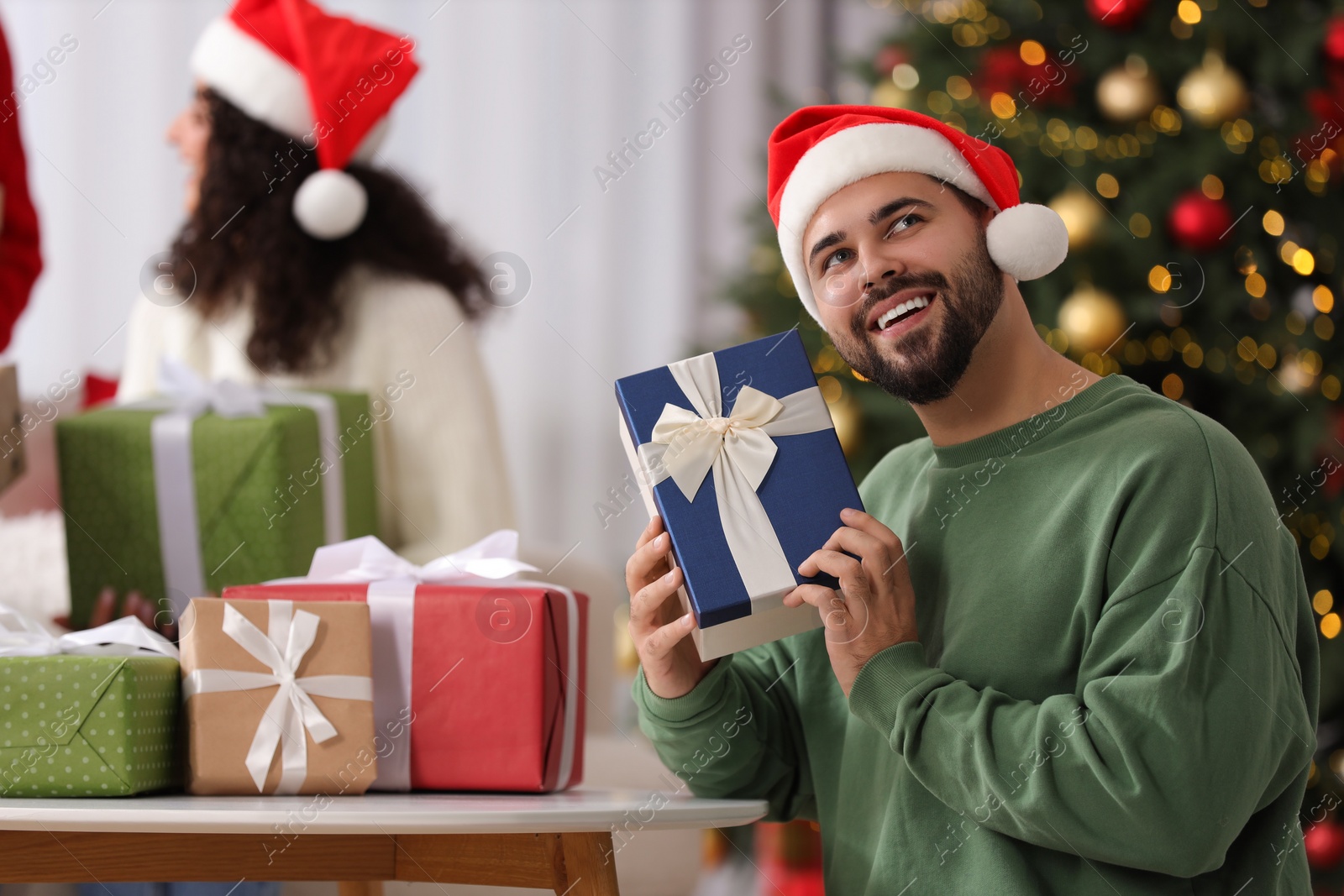 Photo of Christmas celebration in circle of friends. Happy young man with gift box at home, selective focus