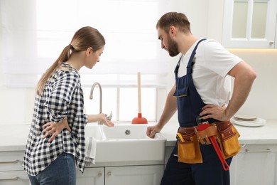 Photo of Young woman complaining to plumber about clogged sink in kitchen
