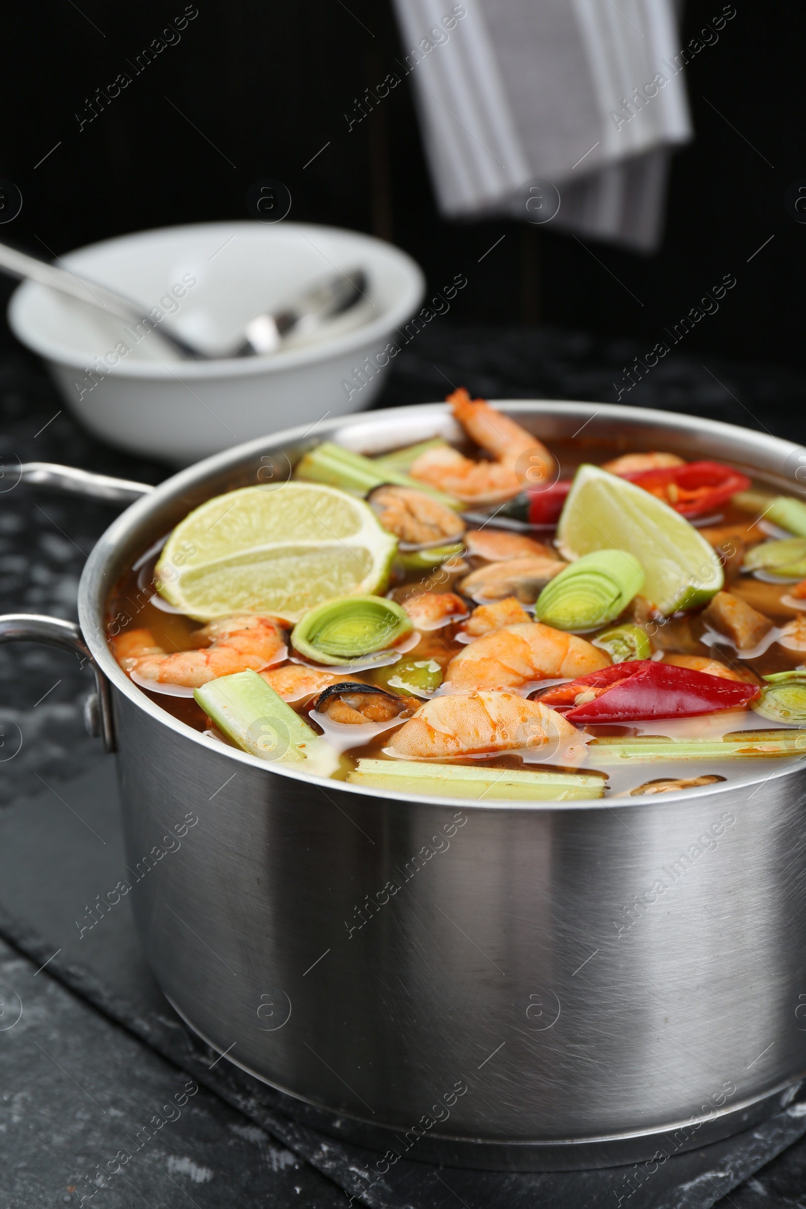 Photo of Saucepan with delicious Tom Yum soup on black marble table, closeup