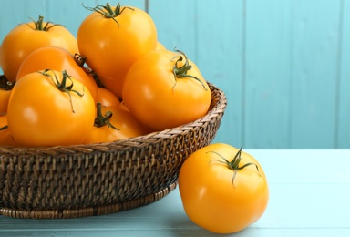 Photo of Ripe yellow tomatoes in wicker bowl on light blue wooden table