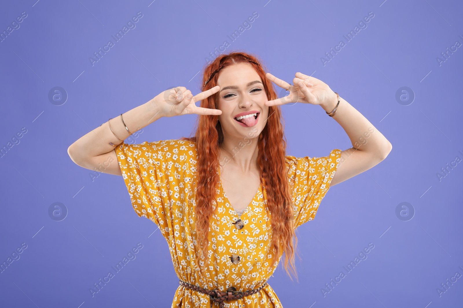 Photo of Beautiful young hippie woman showing V-sign on violet background