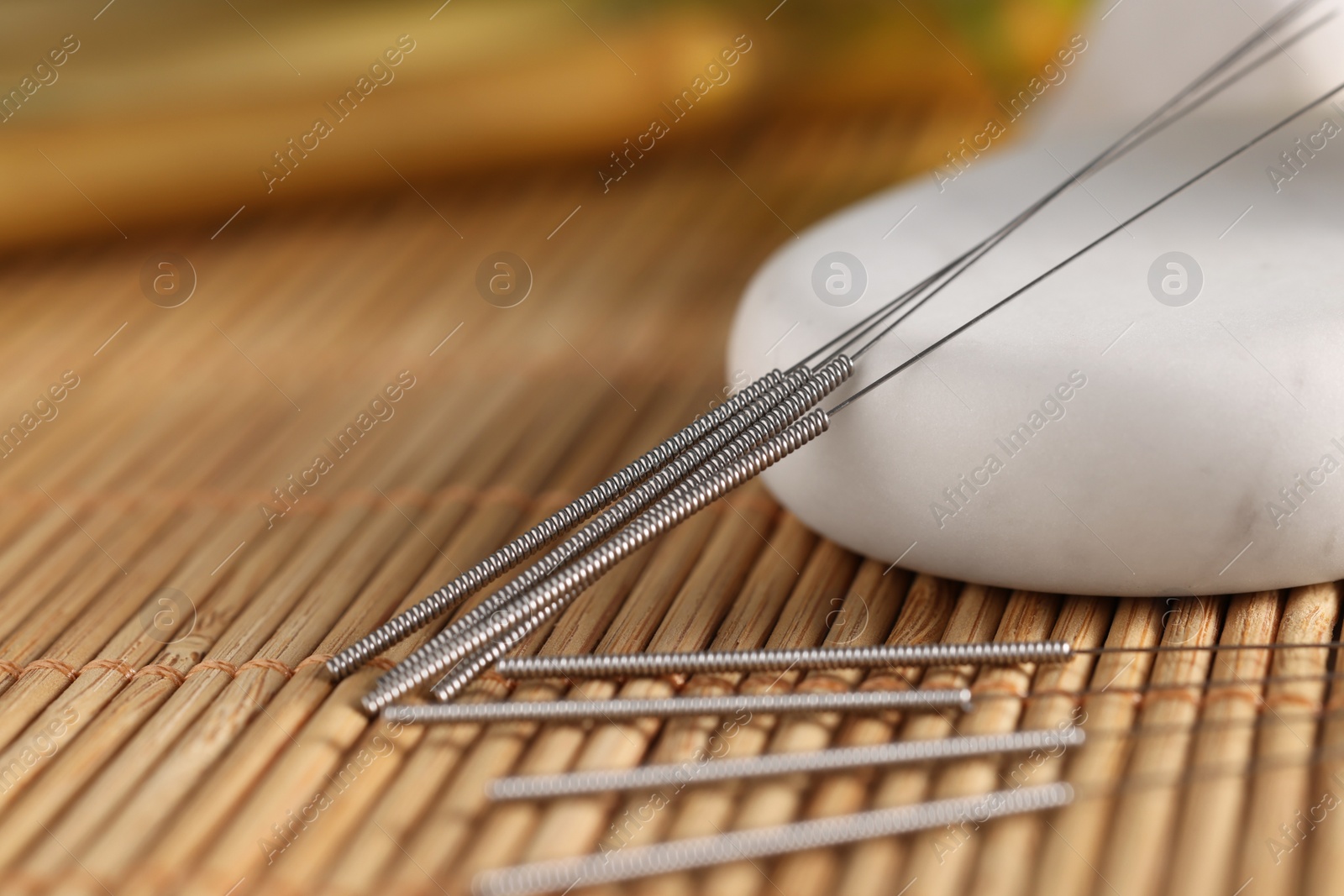 Photo of Acupuncture needles and spa stone on bamboo mat, closeup. Space for text