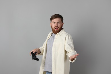 Surprised man with game controller on grey background