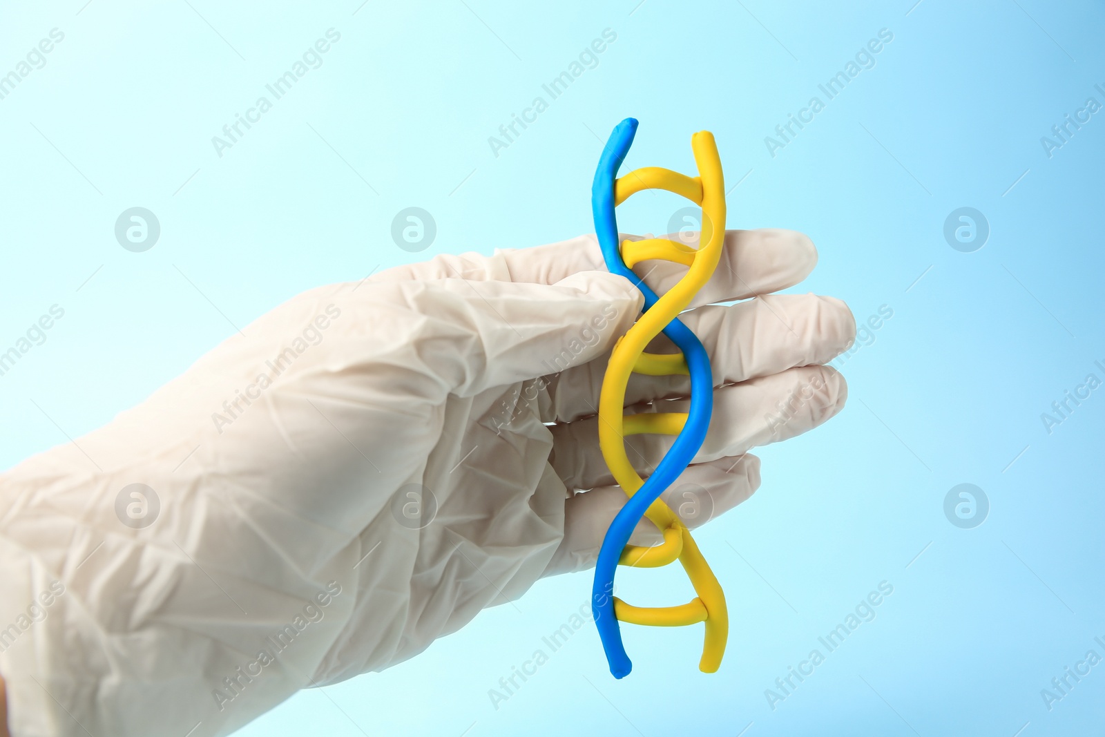 Photo of Scientist with DNA molecule model made of colorful plasticine on light blue background, closeup