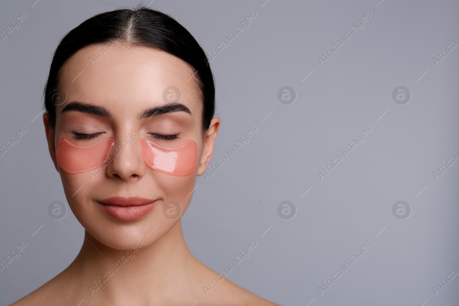 Photo of Beautiful young woman with under eye patches on grey background, space for text