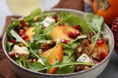 Photo of Tasty salad with persimmon, blue cheese, pomegranate and walnuts served on table, closeup