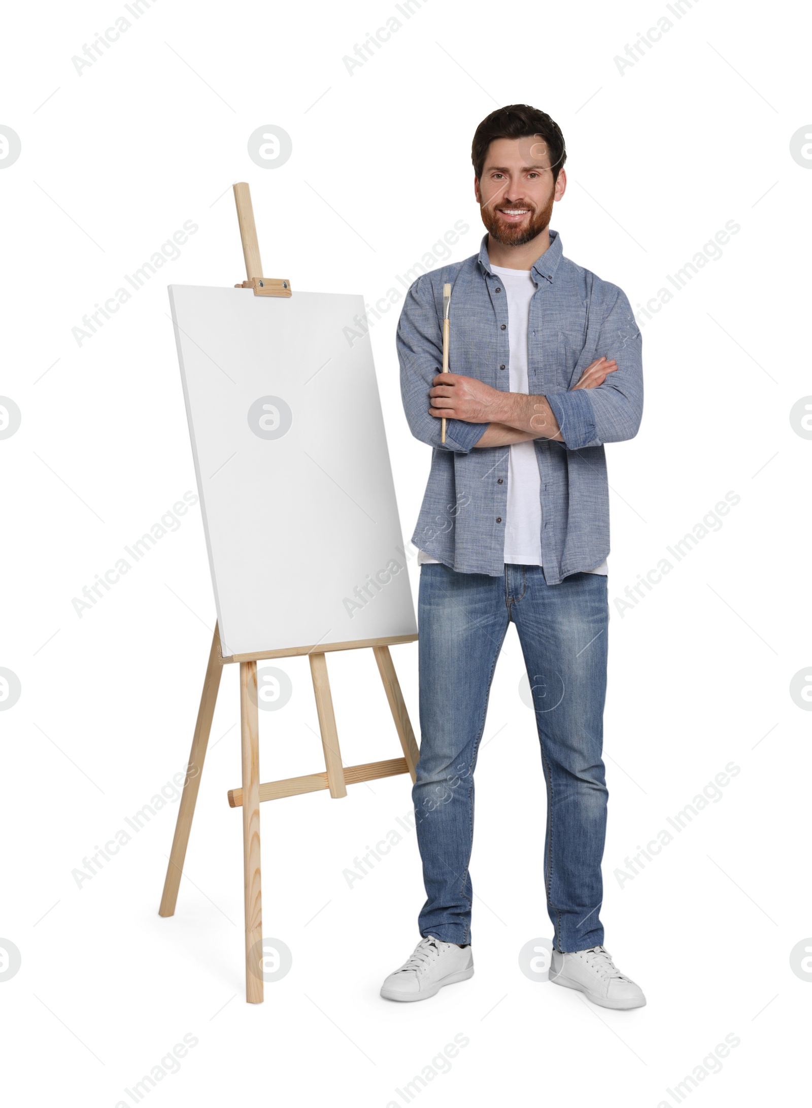 Photo of Happy man with brush near easel with canvas against white background. Creative hobby