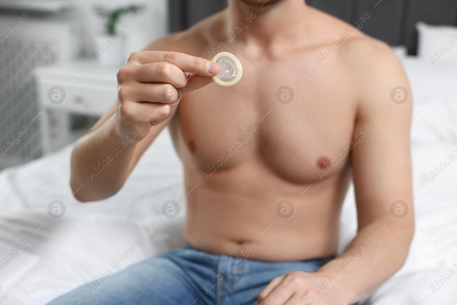 Photo of Closeup view of man showing condom on bed indoors