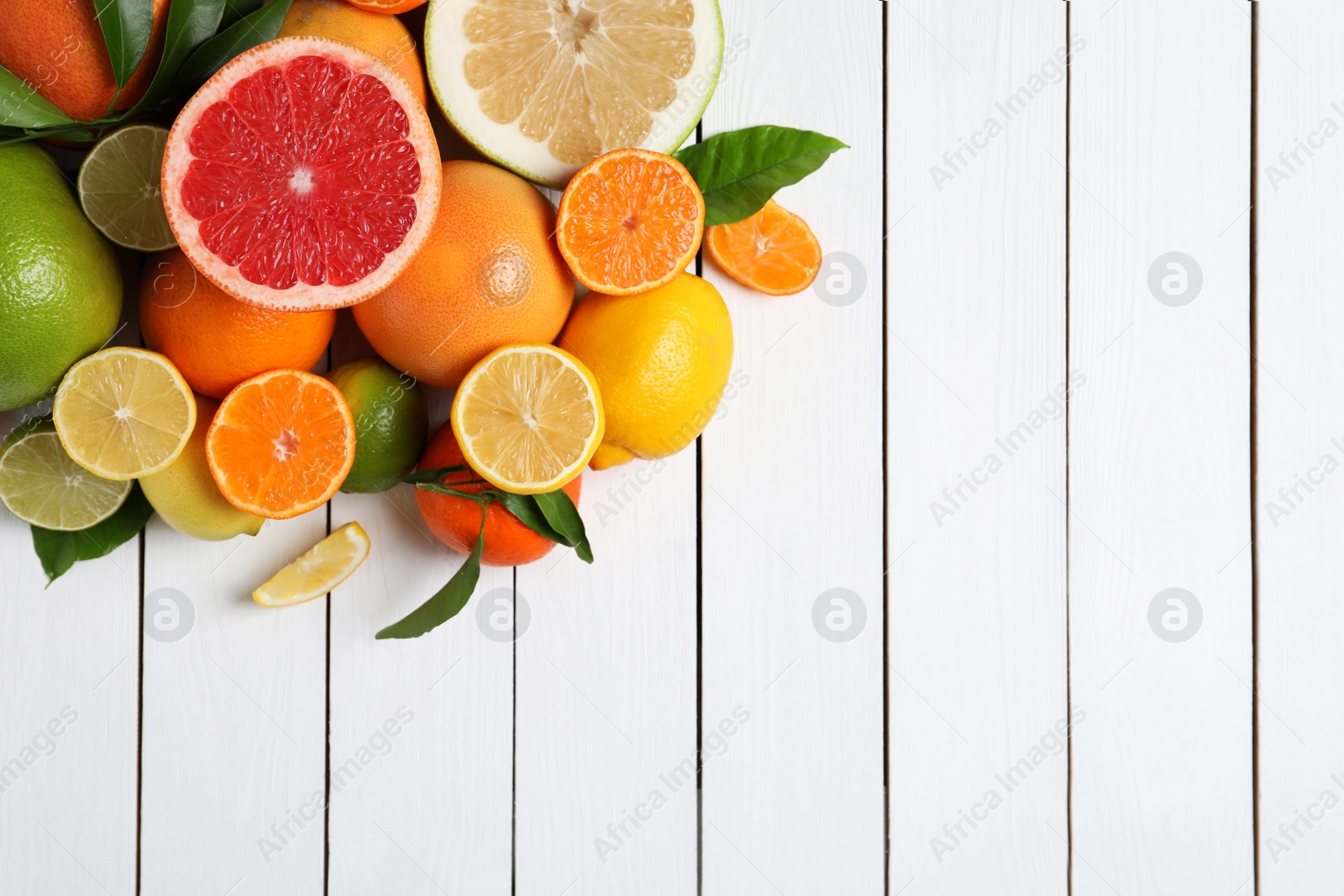 Photo of Different citrus fruits with fresh leaves on white wooden table, flat lay. Space for text