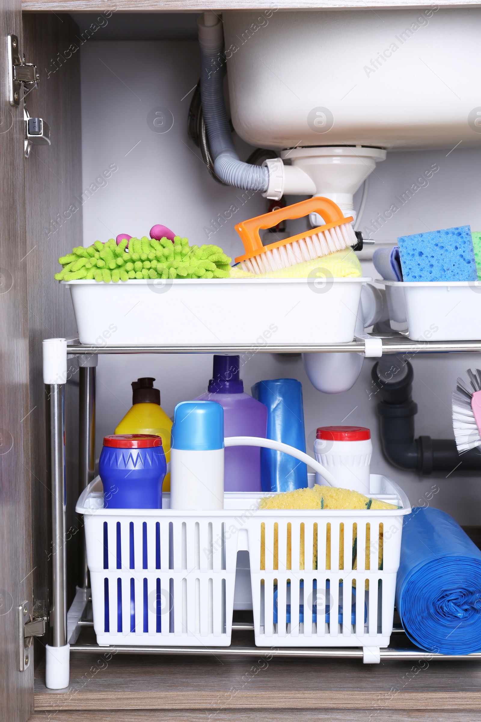 Photo of Open under sink cabinet with different cleaning supplies in kitchen