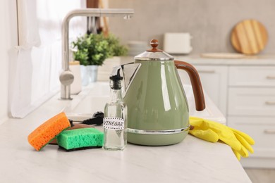 Photo of Cleaning electric kettle. Bottle of vinegar, sponges and rubber glove on countertop in kitchen