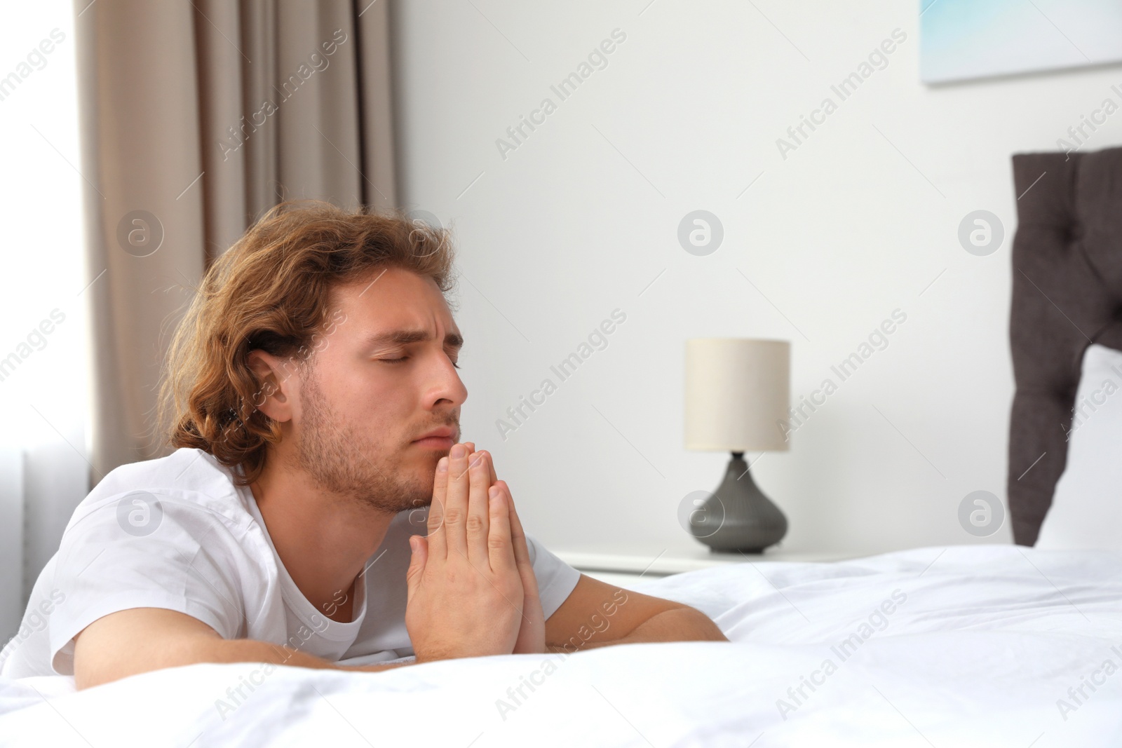 Photo of Handsome young man saying bedtime prayer at home. Space for text