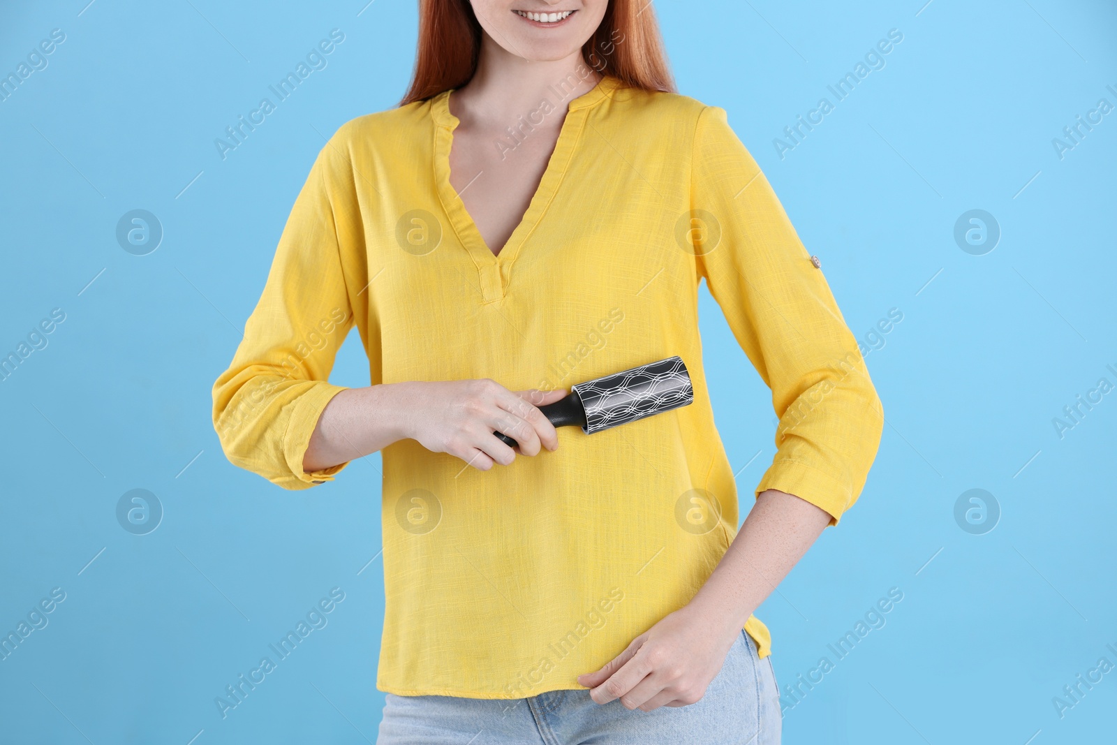 Photo of Young woman cleaning clothes with lint roller on light blue background, closeup