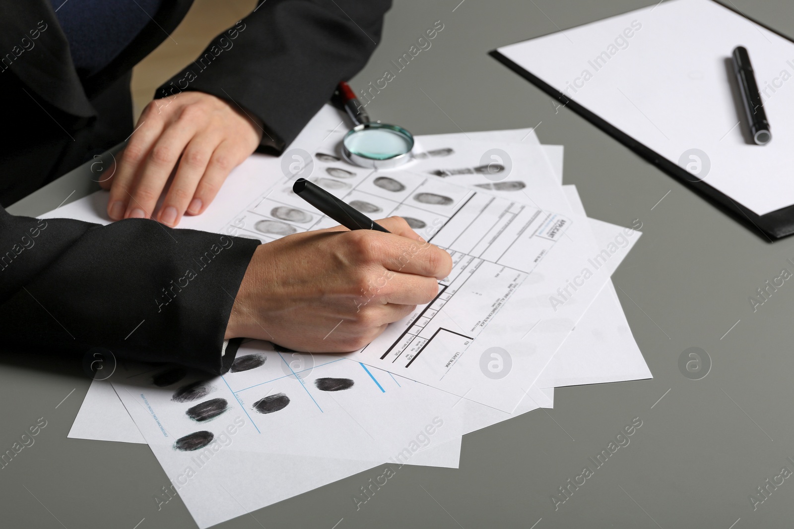 Photo of Female criminalist filling fingerprints card at table, closeup