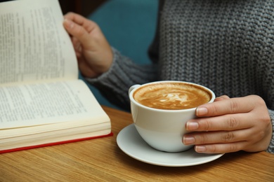 Photo of Woman with cup of coffee reading book at table, closeup