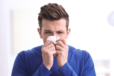 Sad young man with tissue suffering from cold on blurred background