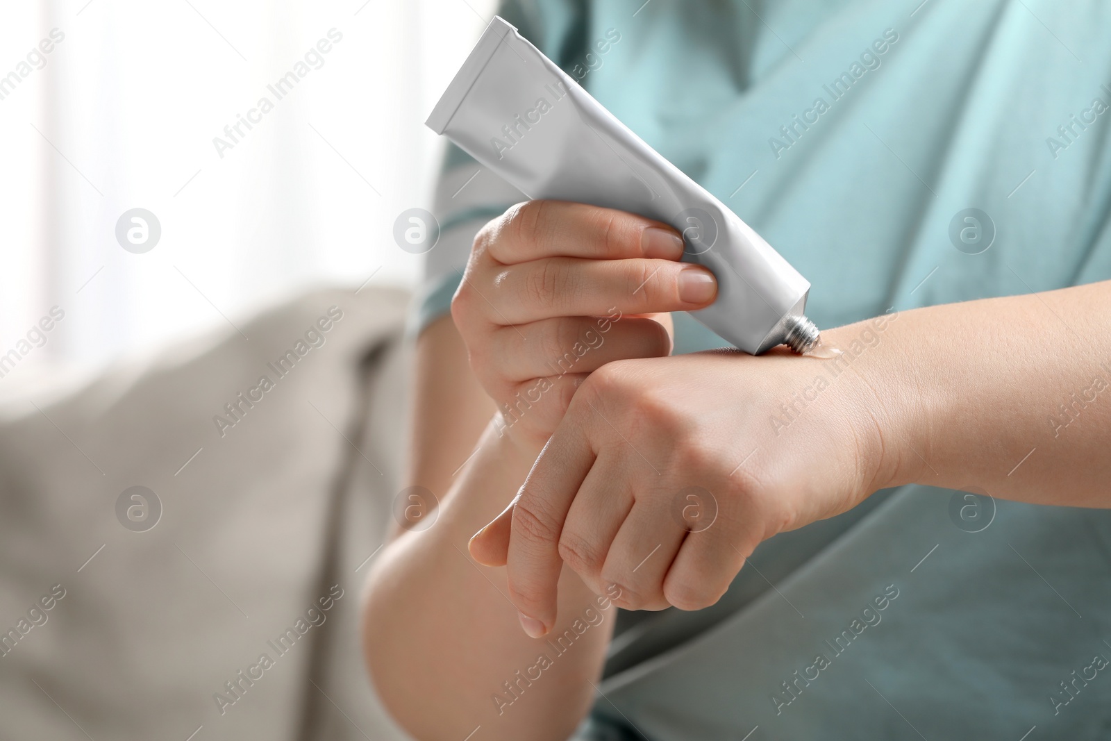 Photo of Woman applying ointment from tube onto her wrist indoors, closeup