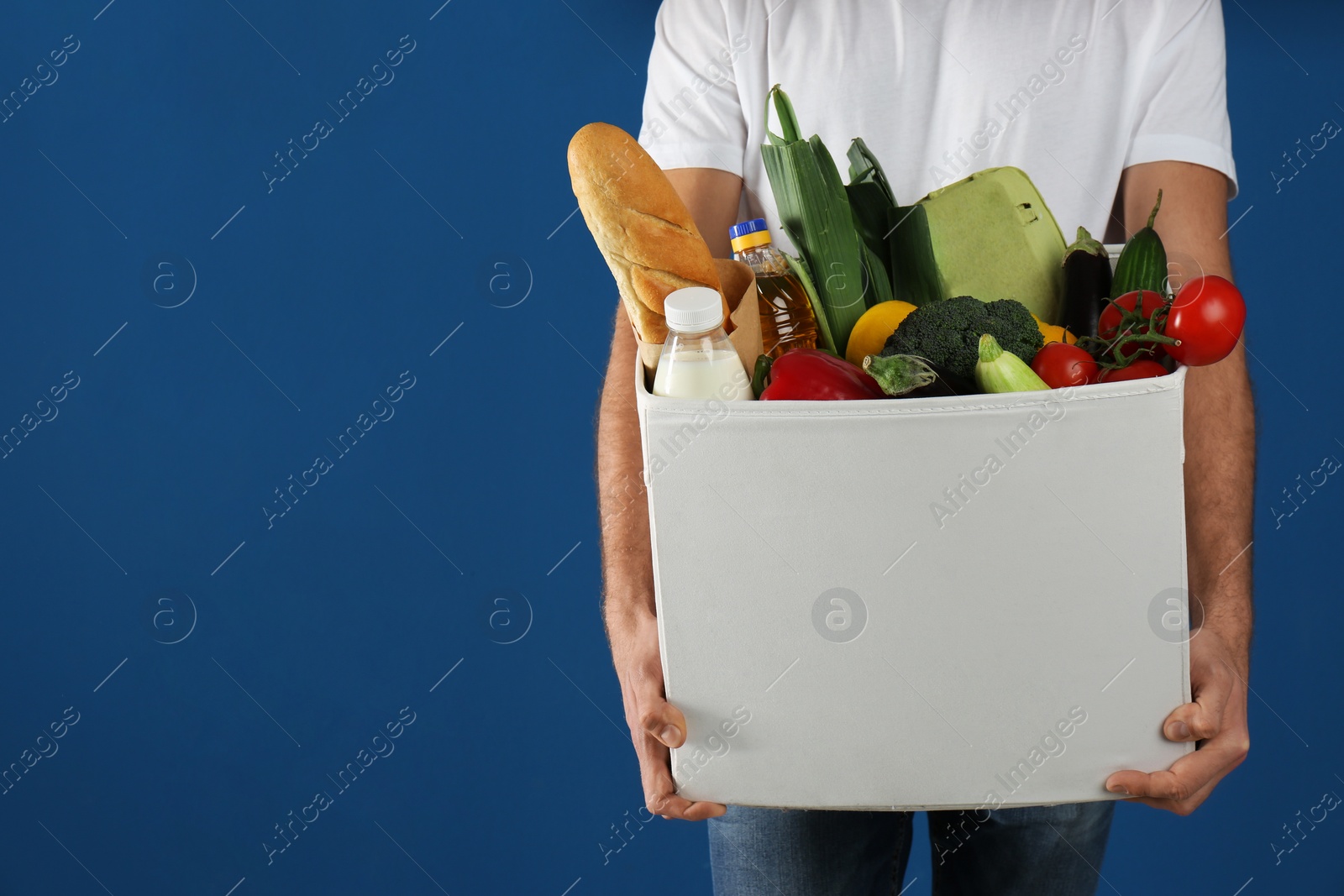 Photo of Courier with fresh products on blue background, closeup. Food delivery service