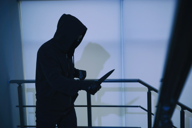 Man in mask with knife on stairs indoors, space for text. Dangerous criminal