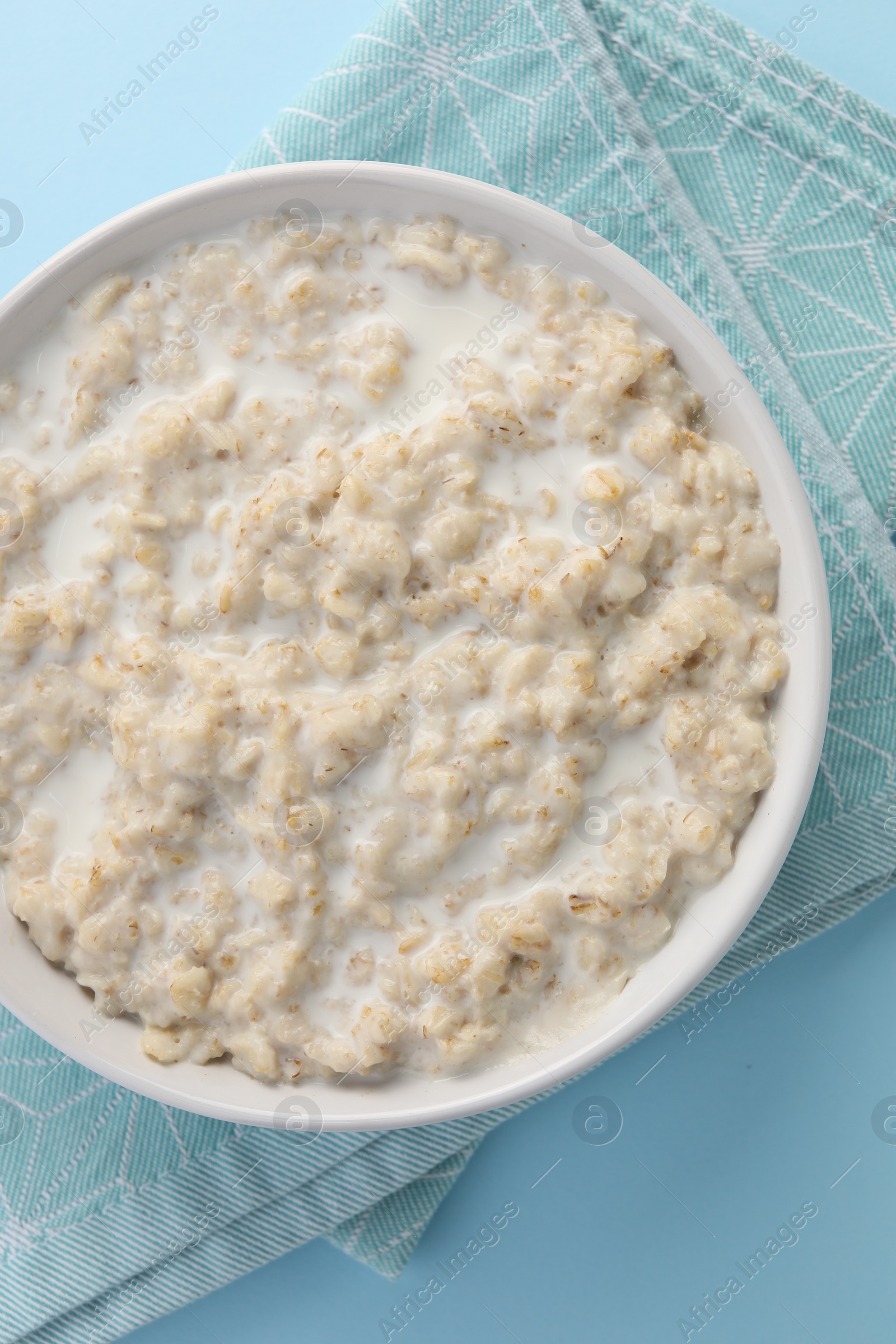 Photo of Tasty boiled oatmeal in bowl on light blue table, top view