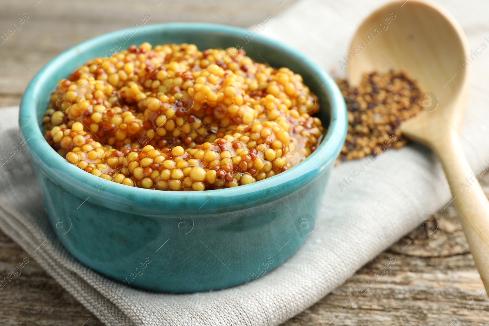 Photo of Fresh whole grain mustard in bowl on wooden table, closeup