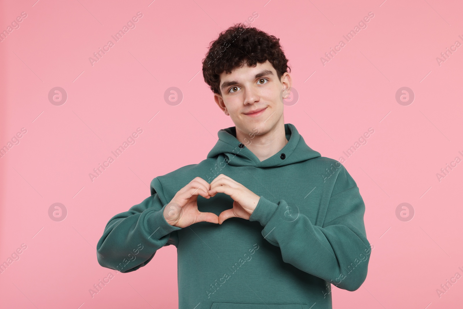 Photo of Happy young man showing heart gesture with hands on pink background