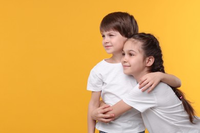 Happy brother and sister on orange background, space for text