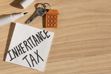 Photo of Inheritance Tax. Paper note, key with key chain in shape of house and marker on wooden table, flat lay. Space for text