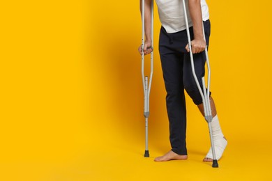 Man with injured leg using crutches on yellow background, closeup. Space for text