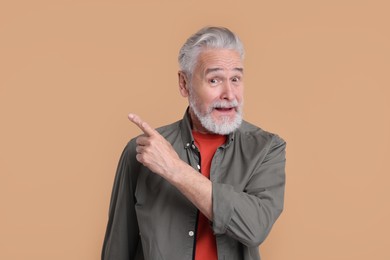 Surprised senior man pointing at something on beige background