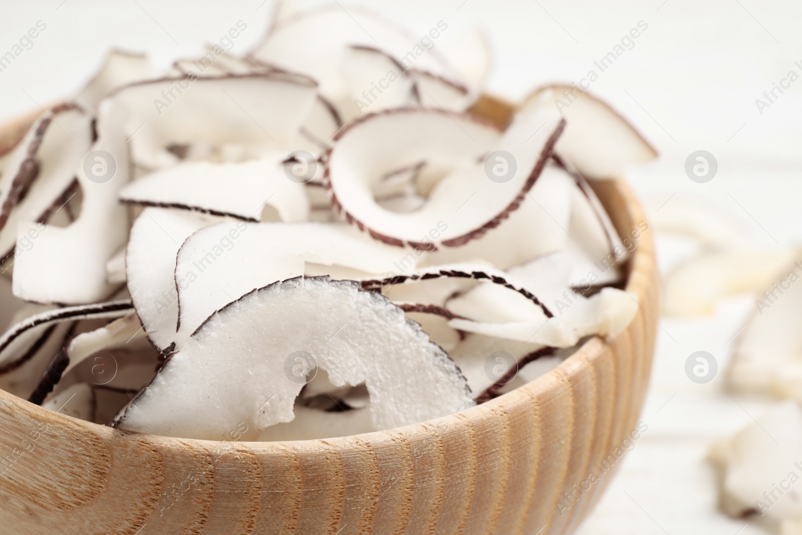Photo of Tasty coconut chips in wooden bowl, closeup