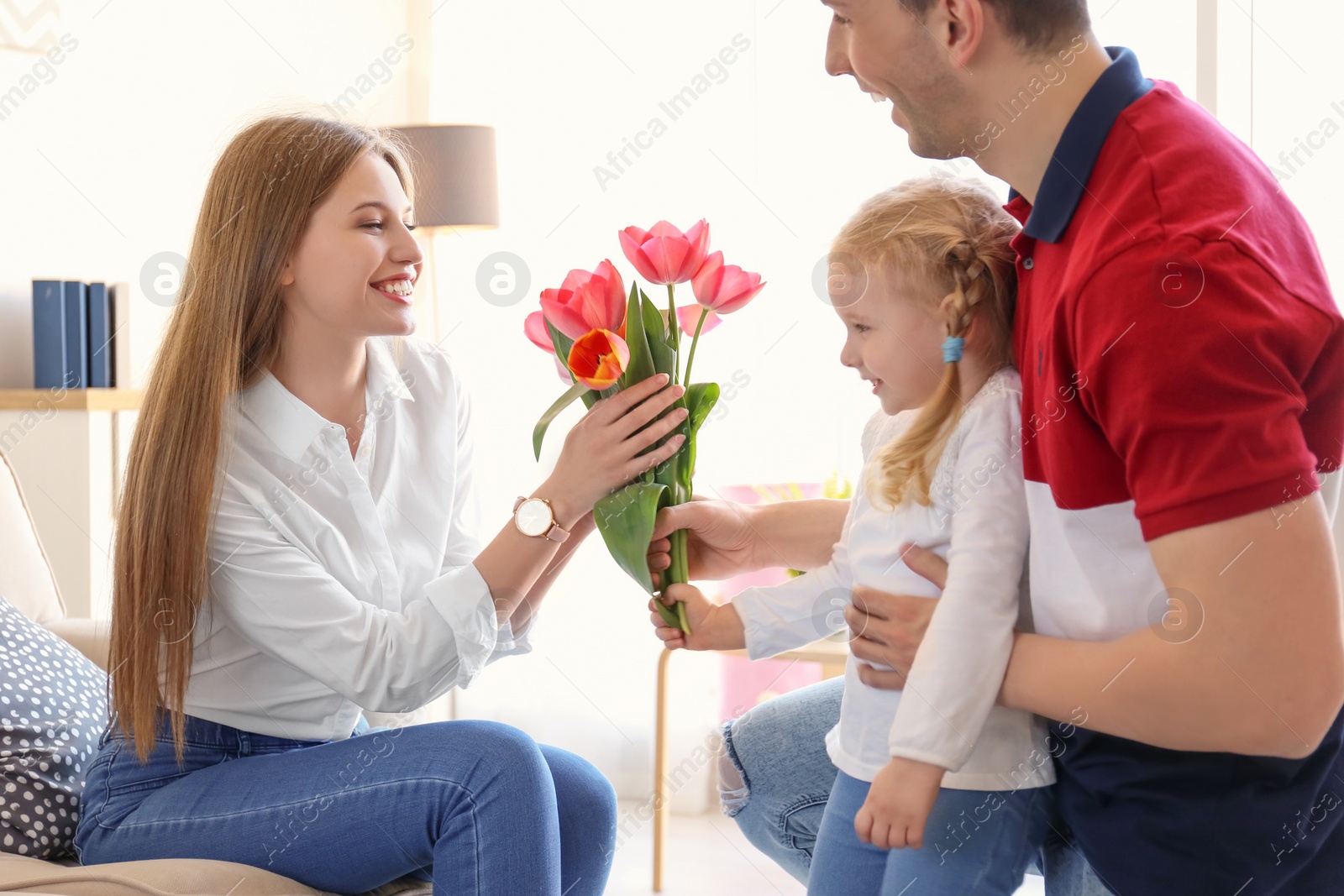 Photo of Happy woman receiving flowers from husband and daughter at home. Mother's day celebration