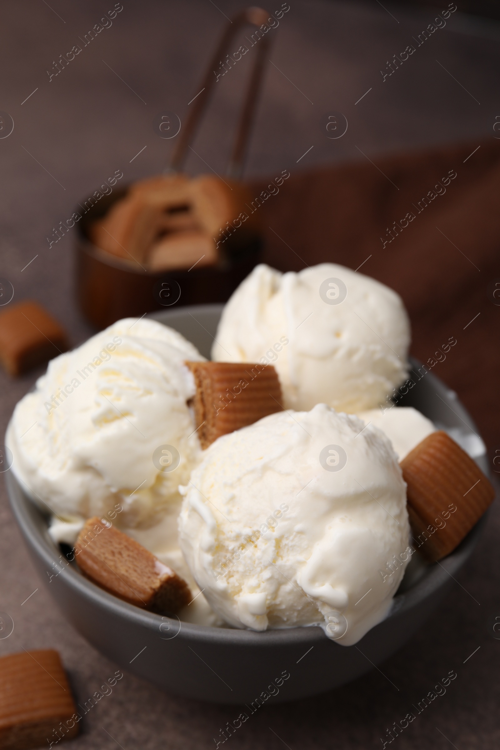 Photo of Scoops of ice cream with caramel candies in bowl on textured table, closeup
