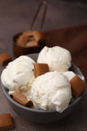 Photo of Scoops of ice cream with caramel candies in bowl on textured table, closeup