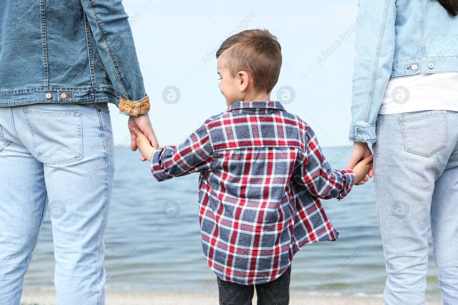 Photo of Little child holding hands with his parents near river. Family time