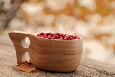 Photo of Cup with tasty lingonberries on wooden table outdoors